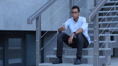 Smartphone kullanarak çevrimiçi gözatmak, genç adam merdivenlerde oturan siyah