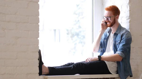 Contestando llamadas telefónicas, Charla de Diseñador, Sentado en la Ventana, Cabellos Rojos y Barba — Foto de Stock