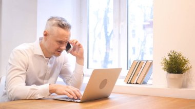 Dizüstü bilgisayarda çalışırken telefon konuşma orta yaş adam tarafından