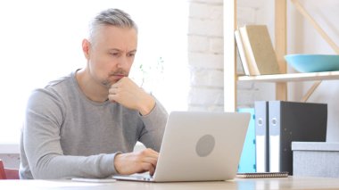 Orta yaşlı adam laptopta düşünüyor ve çalışıyor