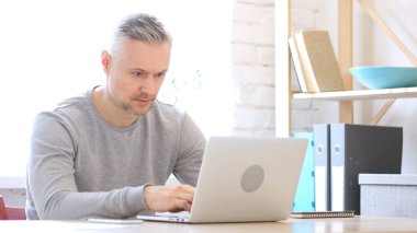 Ofiste dizüstü bilgisayarda çalışan orta yaşlı adam.