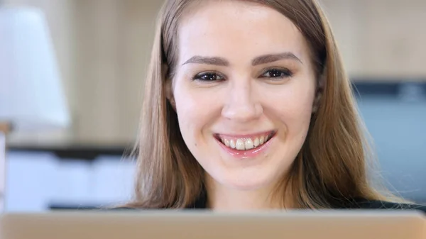 Женщина улыбается перед камерой во время работы над ноутбуком — стоковое фото