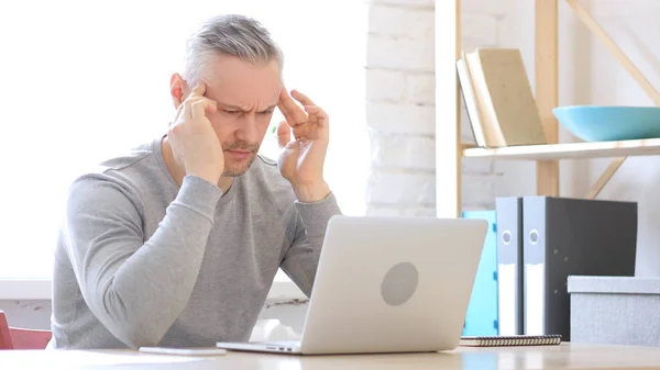 Ból głowy, napięta średnim wieku człowiek pracuje na laptopie — Zdjęcie stockowe