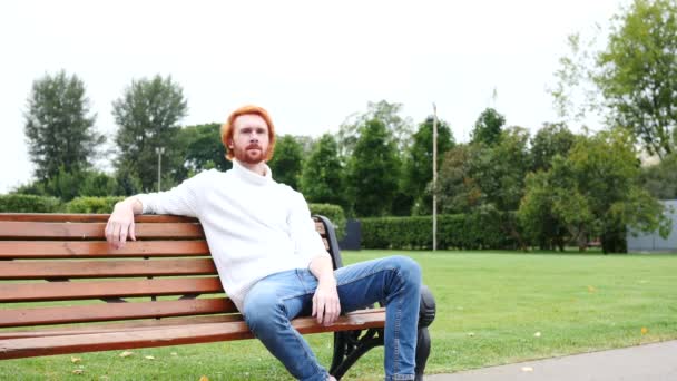 Pulgares hacia arriba por el hombre sentado en el banco en el parque, los cabellos rojos y la barba — Vídeos de Stock