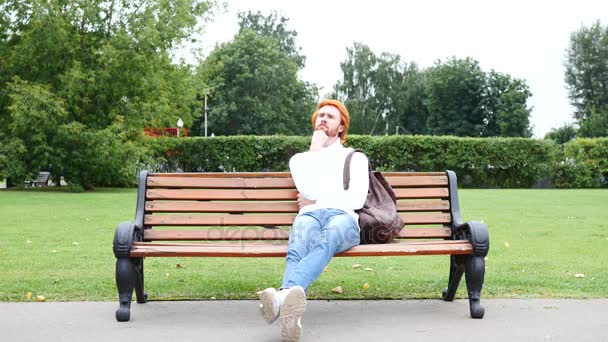 Χαλαρώστε γενειάδα άνθρωπος σκέφτεται ενώ κάθεται στο πάρκο στον πάγκο, κόκκινο τρίχες — Αρχείο Βίντεο
