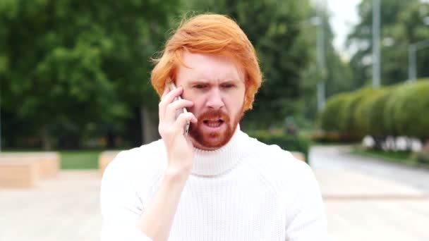 Homem irritado com cabelos vermelhos conversando no telefone no trabalho, ao ar livre — Vídeo de Stock