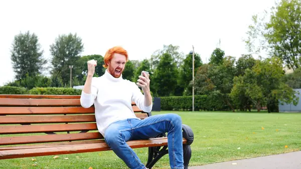 Adam bankta oturan Smartphone kullanarak Successs için heyecanlı