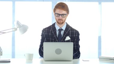 Ofiste dizüstü bilgisayarda çalışan kızıl saçlı adam.