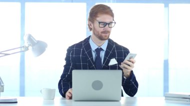 Kızıl saçlı işadamı kullanma Smartphone online iş yerinde tarama,