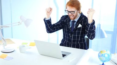 Kızıl saçlı işadamı kutluyor başarı dizüstü bilgisayar, heyecan çalışırken