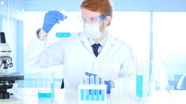 Científico investigador que mira la solución azul en frasco en laboratorio —  Fotos de Stock
