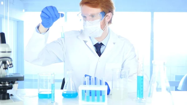 Científico investigador que mira la solución azul en tubo de ensayo en laboratorio —  Fotos de Stock