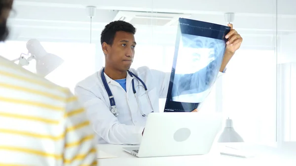 Upset Afro-American Doctor Checking X-ray for Diagnosis, Sick Patient Sitting in Front