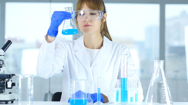 Female Research Scientist Looking at Blue Solution in Flask in Laboratory