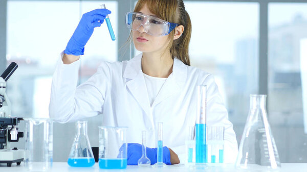 Female Research Scientist Looking at Blue Solution in Test Tube in Laboratory