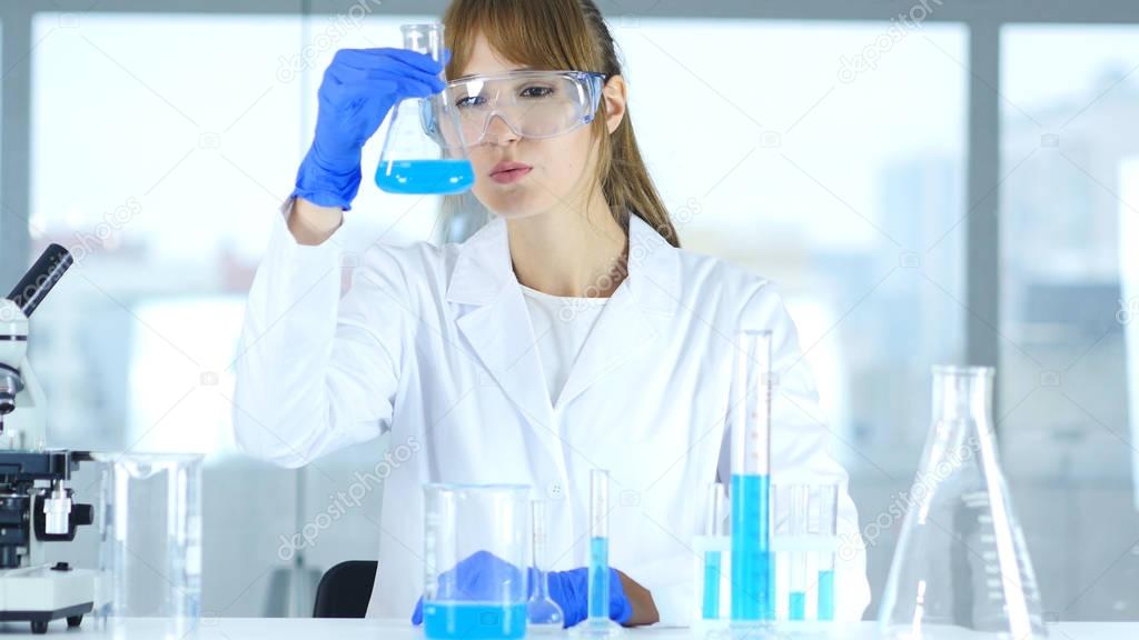 Female Research Scientist Looking at Blue Solution in Flask in Laboratory