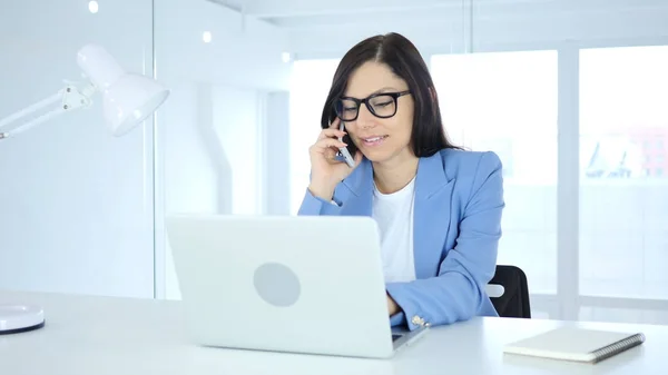 Молодая предпринимательница разговаривает по телефону, посещает телефонный разговор на работе — стоковое фото