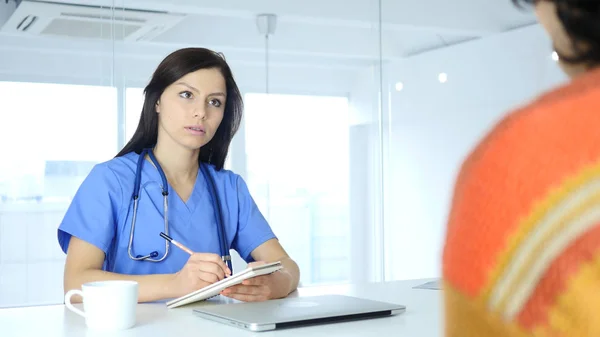 Dokter schrijven geneeskunde en praten met de patiënt, zit — Stockfoto