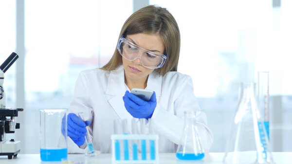 Female Scientist Using Smartphone in Laboratory For Reaction