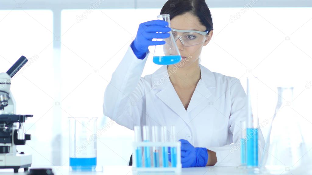 Scientist, Medical Doctor Holding and Looking at Blue Solution in Flask in Laboratory