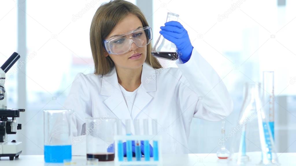 Female Research Scientist Looking at Solution in Beaker in Laboratory, Reaction