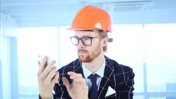 Utilisation de Smartphone au travail, Homme aux cheveux rouges assis au bureau — Video