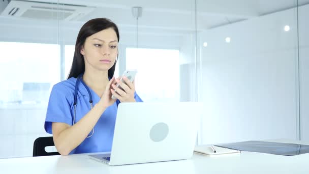 Jonge arts Online browsen op telefoon in het ziekenhuis — Stockvideo