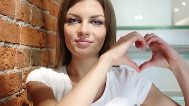 Signo del corazón por las manos, mujer joven sentada en casa — Vídeo de stock