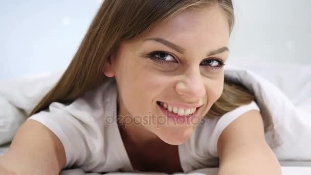 Vacker kvinna i sängen leende och tittar i kameran — Stockvideo