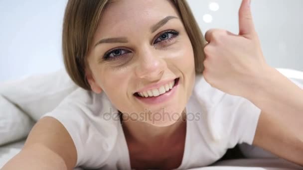 Kciuk w górę przez szczęśliwa Kobieta, leżąc w łóżku, na brzuchu — Wideo stockowe
