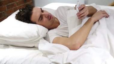 Adam yatak Smartphone'da geceleri tarama.