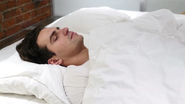 Молодий чоловік спить в ліжку вночі — стокове відео