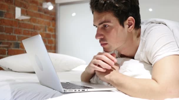 Mann im Bett schockiert über Ergebnisse auf Laptop und fragt sich — Stockvideo