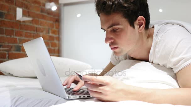 Homem na cama animado para compras online bem sucedidas, transação — Vídeo de Stock