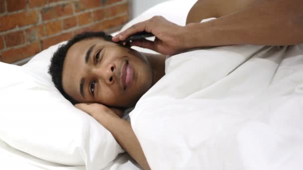 Африканский мужчина лежит в постели и разговаривает по мобильному телефону, переговоры — стоковое видео