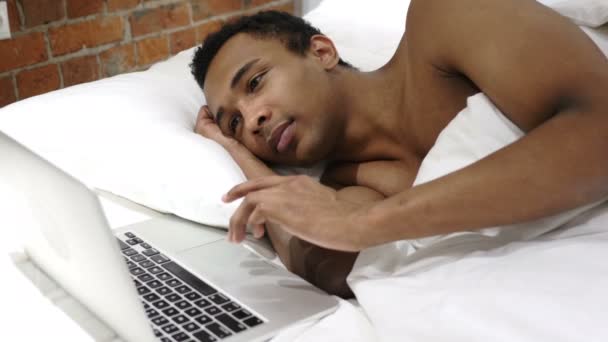 Hombre africano pensativo en la cama Trabajando en el proyecto en el ordenador portátil — Vídeos de Stock