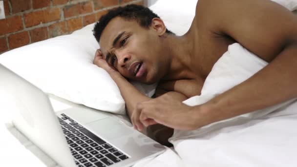 Hombre africano en la cama reaccionando a la pérdida y el fracaso en el ordenador portátil — Vídeos de Stock