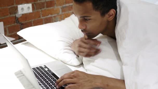 Pensive homme africain couché dans le lit de travail et de réflexion, ordinateur portable — Video