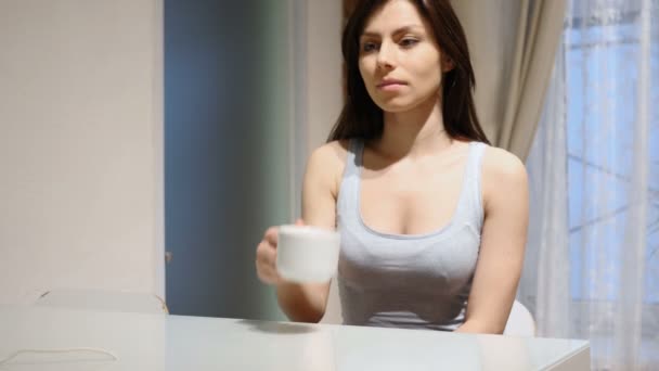 Молода жінка п'є гарячу каву, сидячи вдома — стокове відео