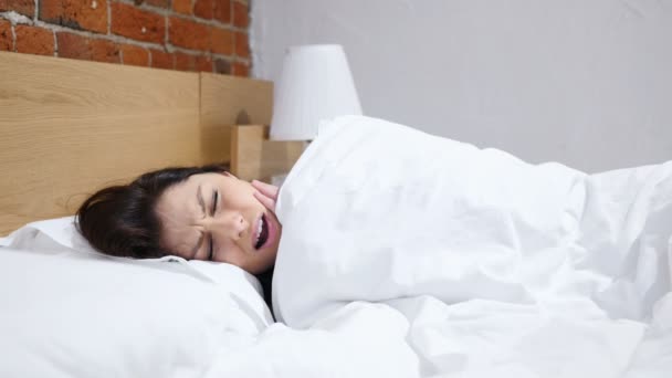 Разочарованная женщина лежит в постели, страдая от боли в зубах, зубной боли — стоковое видео