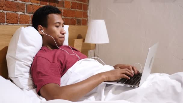 Video Chat pro práci mladý africký muž, ležící v posteli a v noci — Stock video