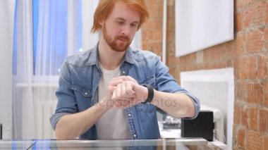 Kızıl saçlı sakallı adam smartwatch kullanarak e-posta ve mesajları gözatmak