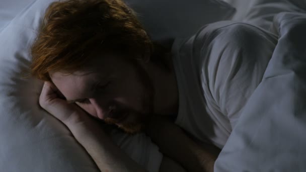 Закрыть лицо молодого рыжеволосого бородатого человека, спящего в кровати — стоковое видео