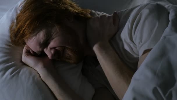 Рыжеволосый бородач с болями в шее пытается спать в постели ночью — стоковое видео