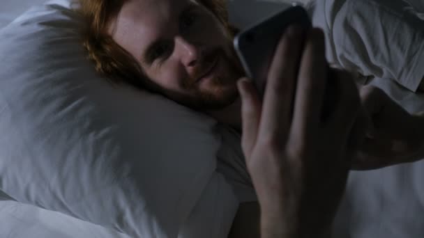 Czat wideo online na Smartphone przez Ruda broda mężczyzna w łóżku — Wideo stockowe