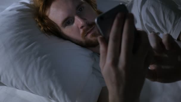 Mann mit rothaarigem Bart surft auf Smartphone, E-Mail und Nachrichten im Bett — Stockvideo