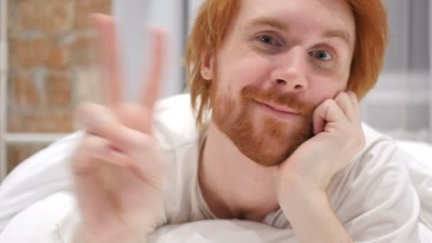 Señal de victoria por Young Redhead Beard Man, gesto positivo en la cama — Vídeo de stock