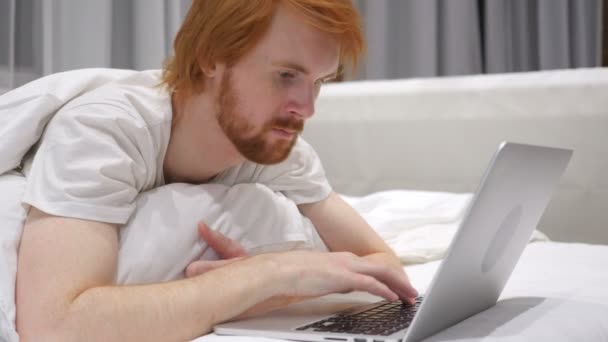 Homem de barba ruiva feliz na cama reagindo ao sucesso do trabalho — Vídeo de Stock