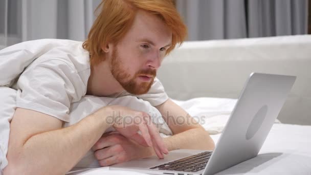 Zavřít se z šoku Redhead vousy muž pracující na notebook v posteli — Stock video