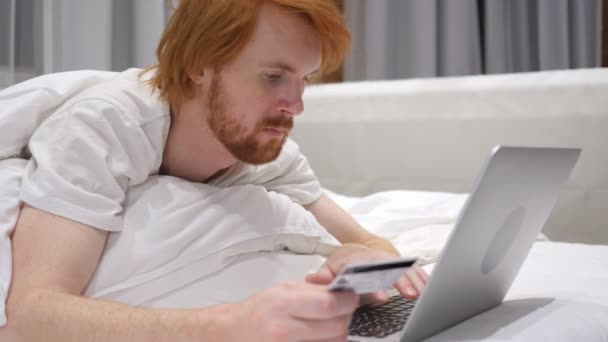 Başarılı Online Kızıl saçlı sakallı adam yatakta, kredi kartı ile alışveriş — Stok video